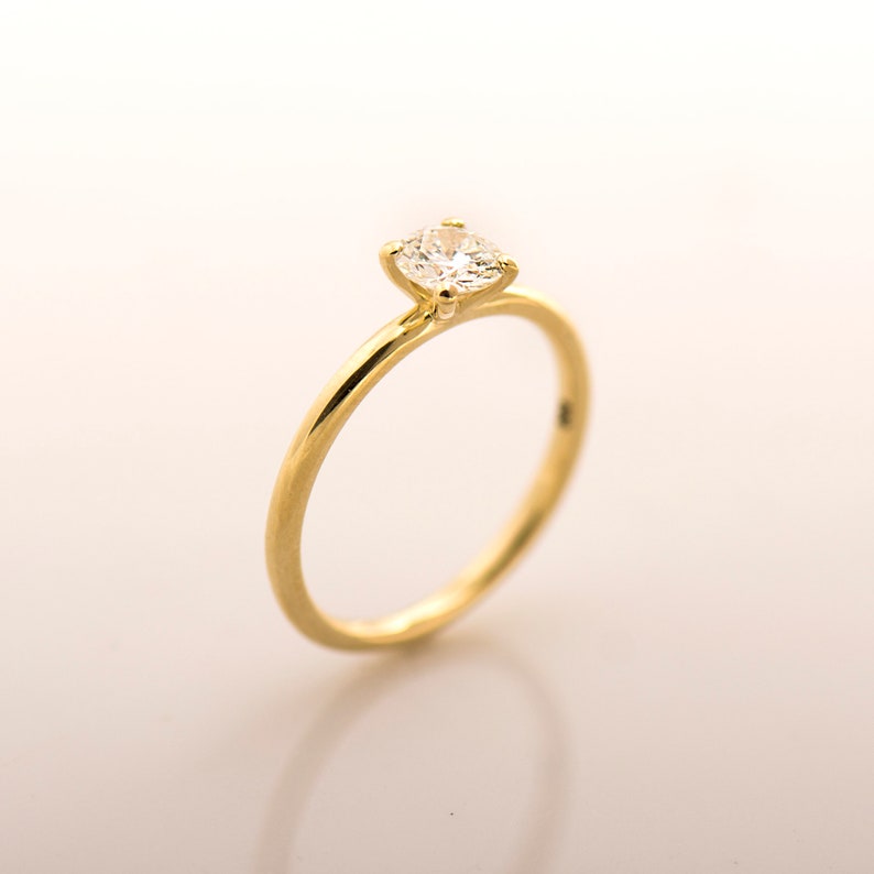 May include: A simple gold band engagement ring with a single round diamond.