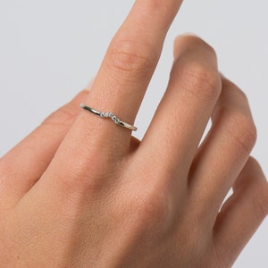 May include: A delicate silver ring with a curved band and small diamonds set in the center.