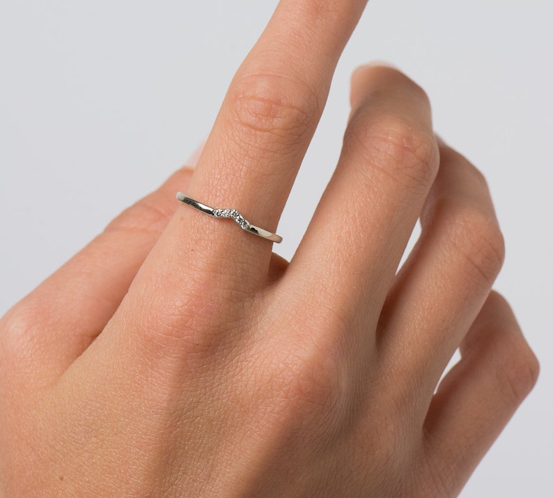 May include: A delicate silver ring with a curved band and small diamonds set in the center.