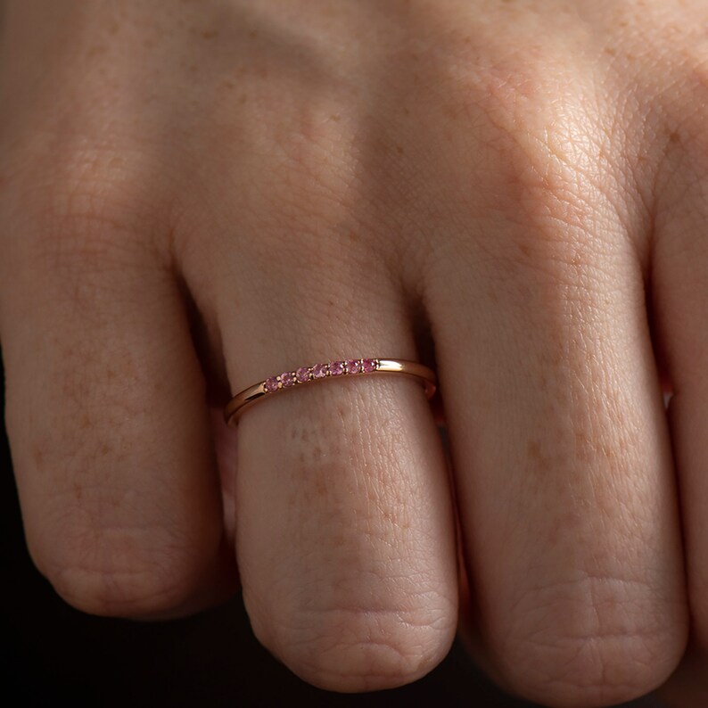 May include: A delicate gold band ring with a row of small pink gemstones.