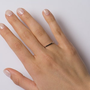 Peut inclure: Une d&eacute;licate bague en argent avec une rang&eacute;e de petits diamants noirs.