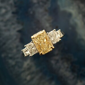 May include: A gold ring with a large, rectangular, yellow diamond in the center and two smaller, square, clear diamonds on either side.