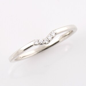 May include: A delicate silver band with a row of small diamonds set in a chevron pattern.