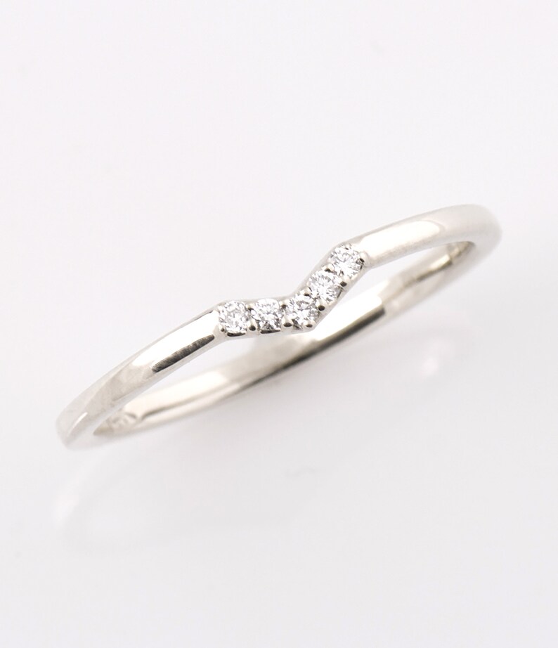 May include: A delicate silver band with a row of small diamonds set in a chevron pattern.