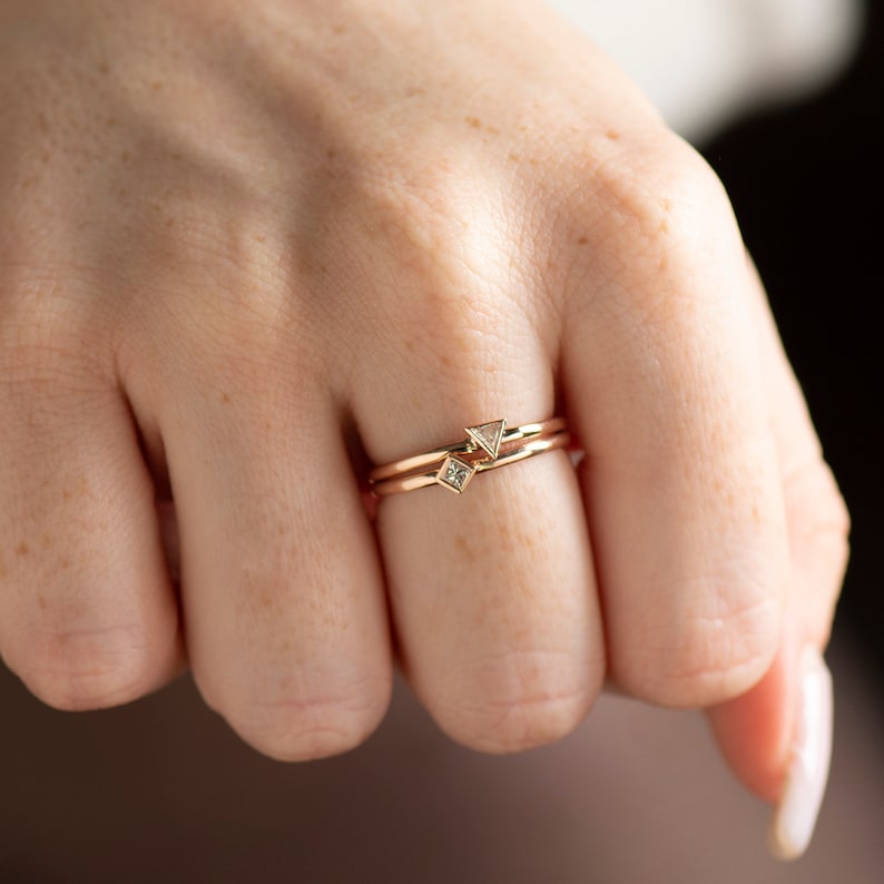 May include: Two gold rings with small diamond accents. The rings are stacked on a finger.