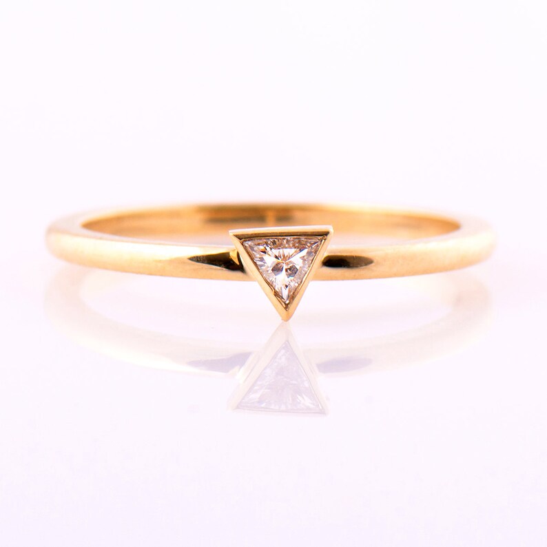 May include: A simple gold band ring with a small triangular diamond set in a triangular prong setting.