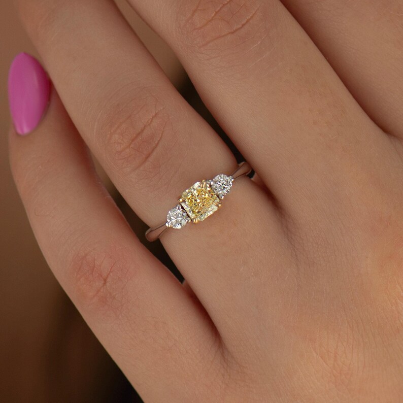 K&ouml;nnte beinhalten: Ein dreisteiniger Ring mit einem gelben Diamanten in der Mitte und zwei kleineren wei&szlig;en Diamanten auf jeder Seite. Der Ring ist in Wei&szlig;gold gefasst.