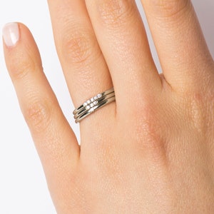 Op de afbeelding: Een set van drie dunne gouden ringen met een rij kleine diamanten op de bovenste ring.
