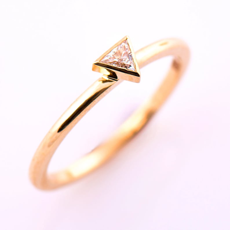May include: A gold band ring with a small triangular diamond set in the center.