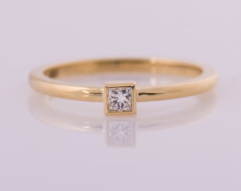 May include: A simple gold band ring with a single square-shaped diamond set in the centre.