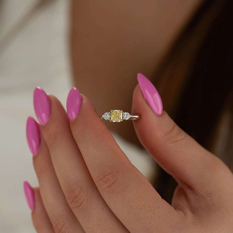 K&ouml;nnte beinhalten: Ein goldener Ring mit einem gelben Diamanten in der Mitte und zwei kleineren Diamanten an den Seiten.