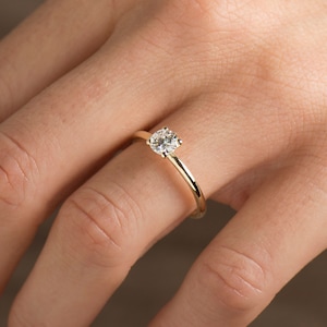 May include: A simple gold band engagement ring with a single round diamond.