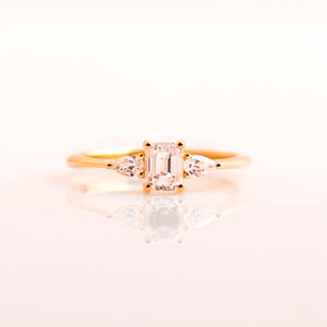 May include: A gold ring with a large emerald-cut diamond and two smaller pear-shaped diamonds on either side.