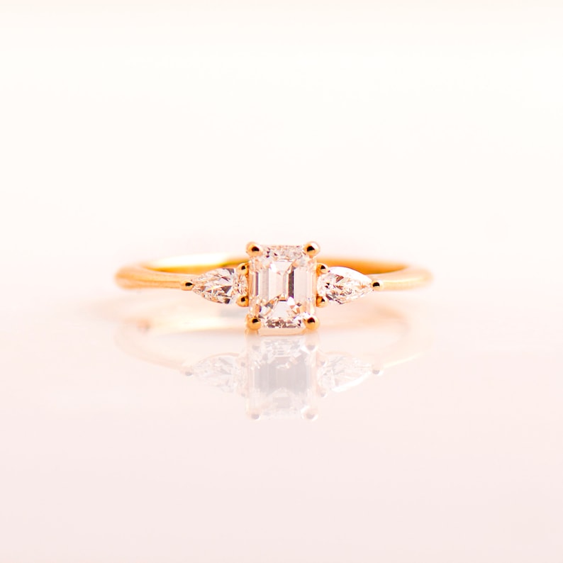 May include: A gold ring with a large emerald-cut diamond and two smaller pear-shaped diamonds on either side.