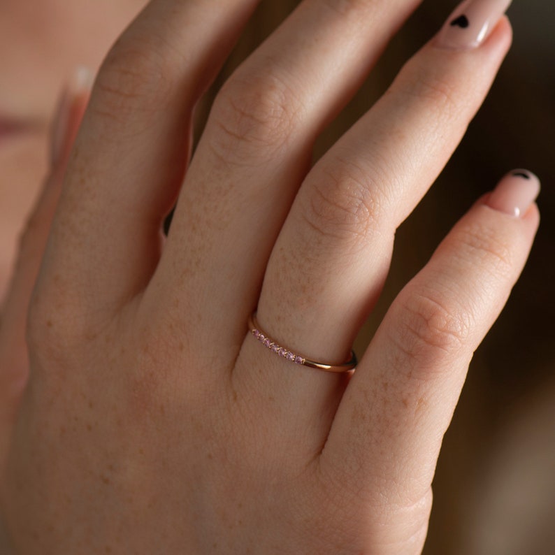 May include: A delicate rose gold band ring with a row of small pink gemstones.