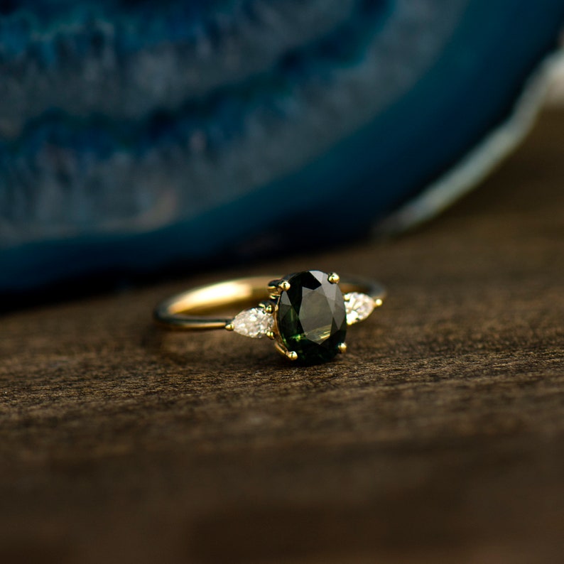 May include: A gold ring with a dark green oval gemstone and two smaller pear-shaped diamonds on either side.