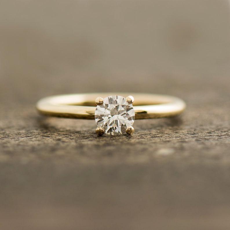 May include: A gold band engagement ring with a round, clear diamond.