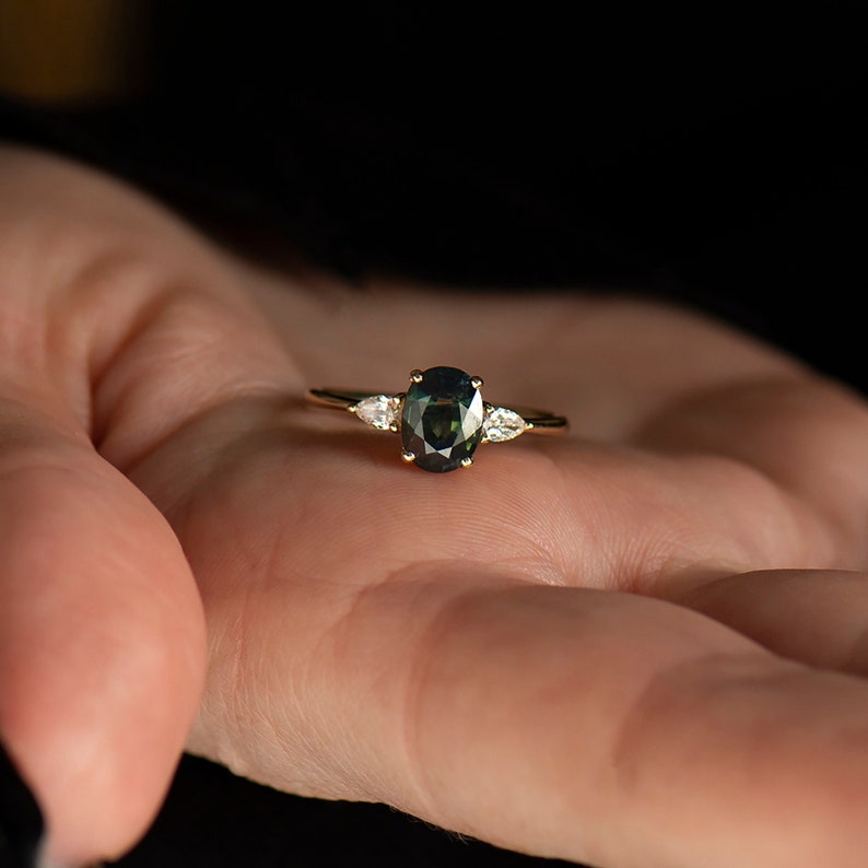 May include: A gold ring with a dark green oval gemstone and two smaller pear-shaped diamonds on either side.