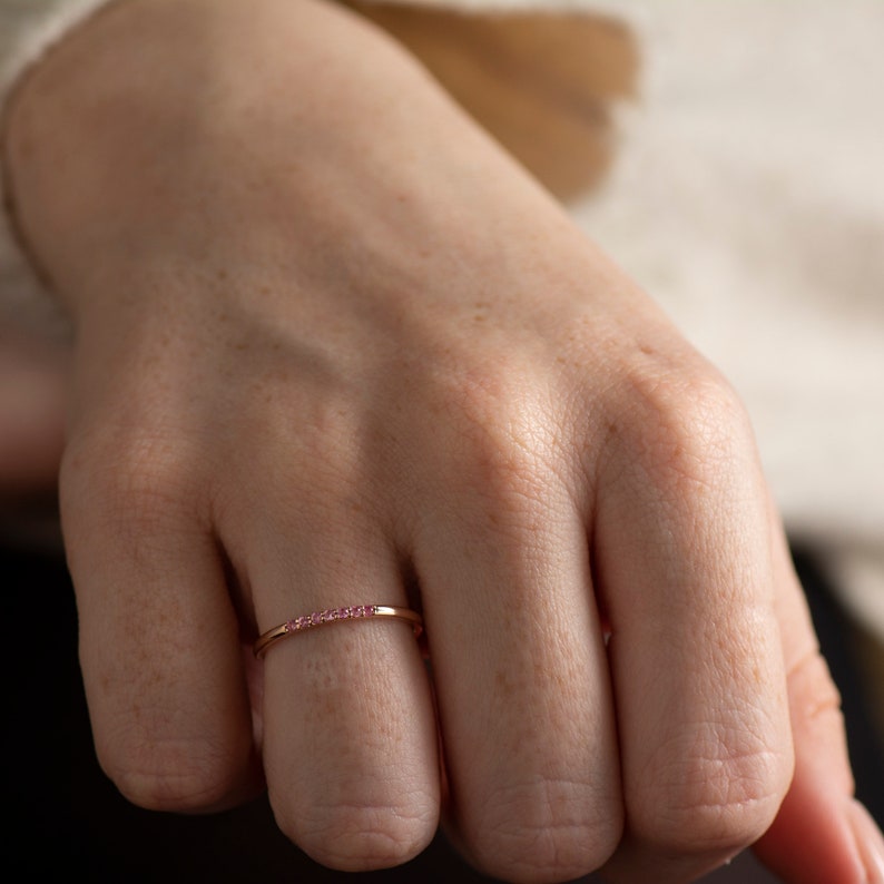 May include: A delicate gold band ring with a row of small pink gemstones.