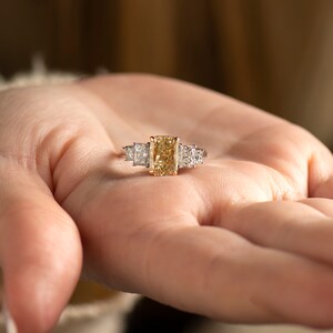 May include: A gold ring with a large, rectangular, yellow diamond in the center and two smaller, square, white diamonds on either side.