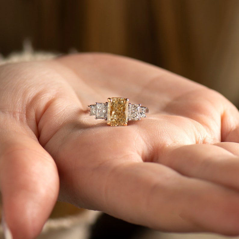 May include: A gold ring with a large, rectangular, yellow diamond in the center and two smaller, square, white diamonds on either side.