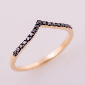 May include: A gold band ring with a row of black diamonds set in a V-shape.