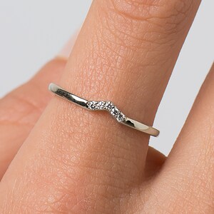 May include: A delicate silver ring with a curved band and a row of small diamonds.
