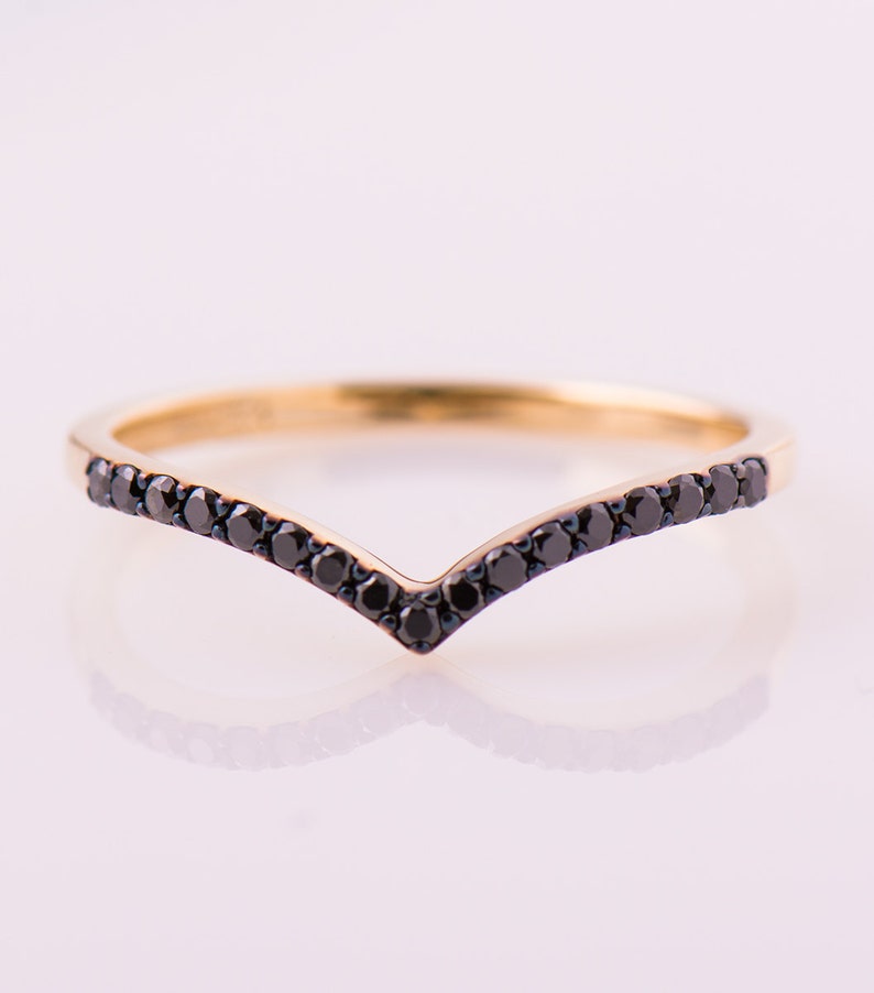 May include: A gold band ring with a V-shaped row of black diamonds.