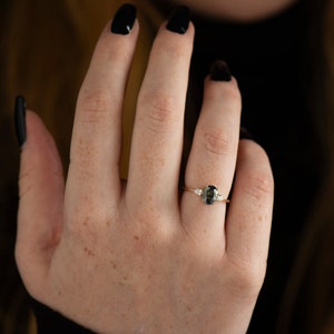 May include: A gold ring with a dark green oval gemstone and two smaller white gemstones on either side.