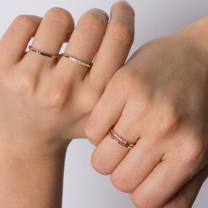 May include: Three gold rings with different colored stones. The first ring has black stones, the second has white stones, and the third has pink stones.