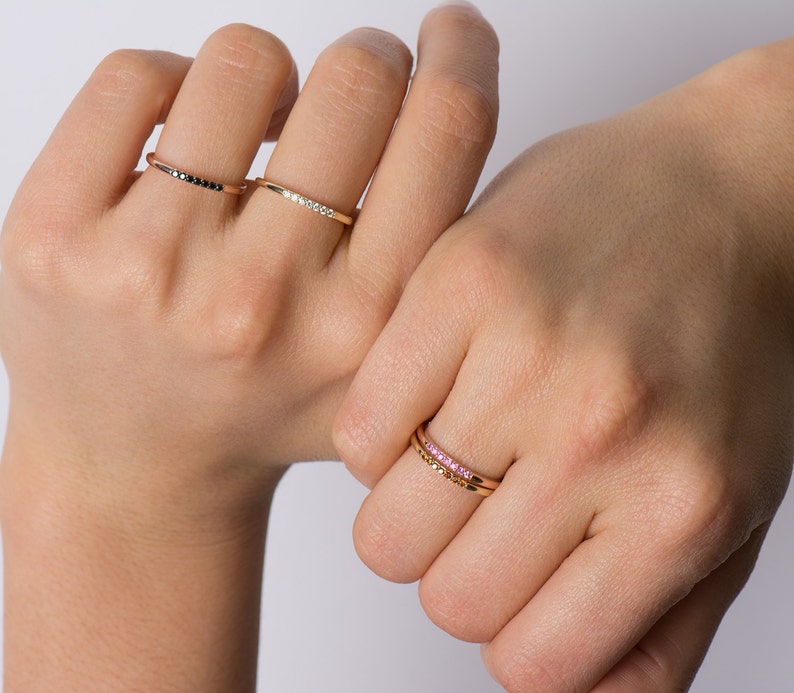 May include: Three gold rings with different colored stones. The first ring has black stones, the second has white stones, and the third has pink stones.