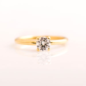 May include: A gold band ring with a single round diamond set in the center.