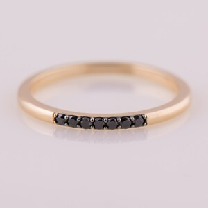 May include: A thin gold band ring with a row of black diamonds set in the center.