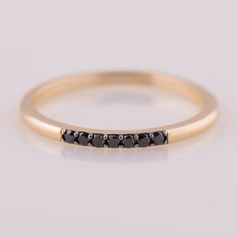 May include: A thin gold band ring with a row of black diamonds set in the center.