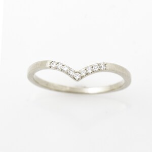 May include: A delicate silver band ring with a V-shaped row of small diamonds.
