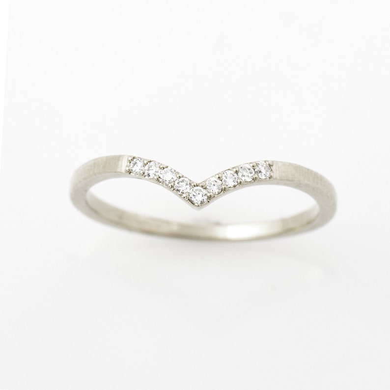 May include: A delicate silver band ring with a V-shaped row of small diamonds.