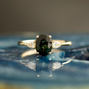May include: A gold ring with a large oval green gemstone and two smaller pear-shaped diamonds on either side.
