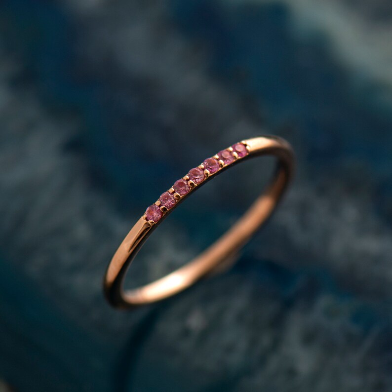 May include: A delicate gold band ring with a row of small pink gemstones.