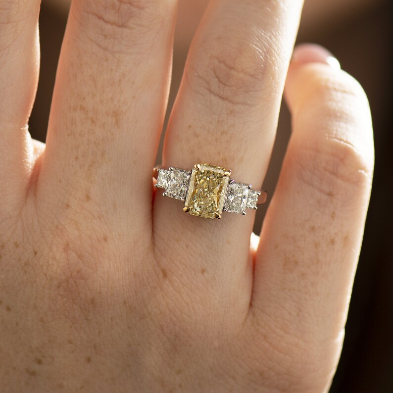 May include: A gold ring with a large, rectangular, yellow diamond in the center and two smaller, square, white diamonds on either side.