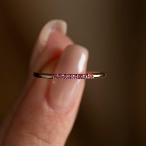 May include: A delicate gold band ring with a row of small pink gemstones.