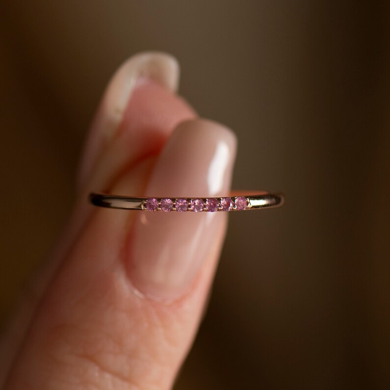 May include: A delicate gold band ring with a row of small pink gemstones.