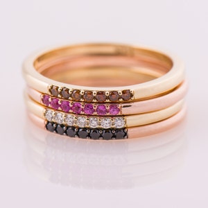 Peut inclure: Quatre bagues empilables en or avec des pierres pr&eacute;cieuses de diff&eacute;rentes couleurs. La bague du haut a des pierres brunes, la deuxi&egrave;me bague a des pierres roses, la troisi&egrave;me bague a des pierres claires et la bague du bas a des pierres noires.