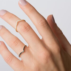May include: Two gold rings with a V-shaped design. One ring is set with white diamonds and the other with black diamonds.