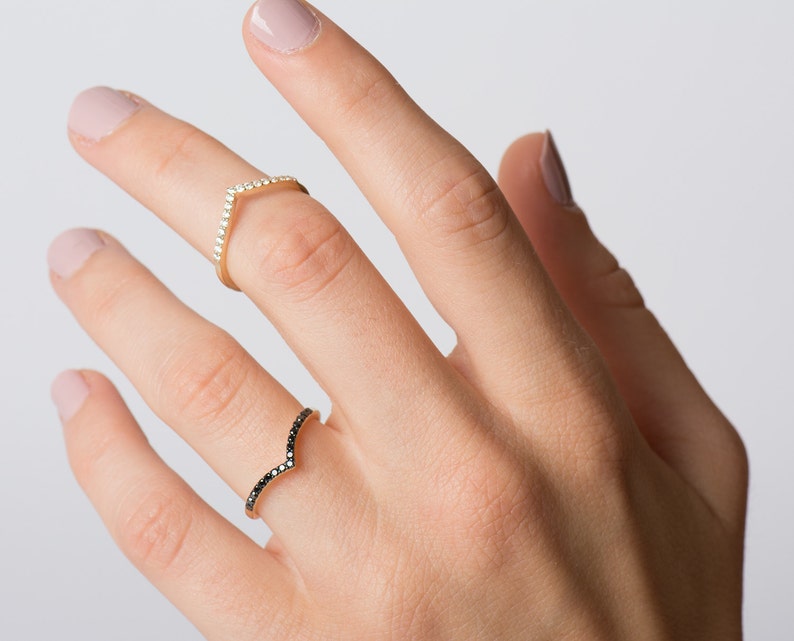 May include: Two gold rings with a V-shaped design. One ring is set with white diamonds and the other with black diamonds.