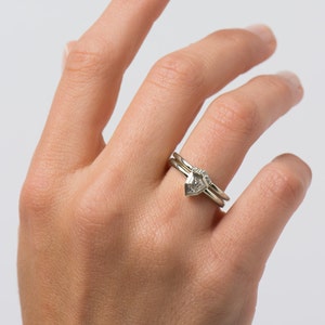 May include: A set of two silver rings with a pear-shaped diamond on the top ring. The diamond is set in a prong setting and has a small diamond on each side.