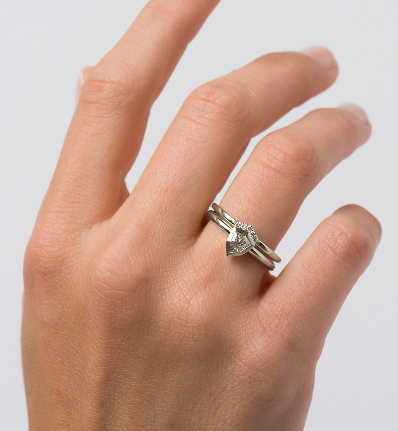 May include: A set of two silver rings with a pear-shaped diamond on the top ring. The diamond is set in a prong setting and has a small diamond on each side.