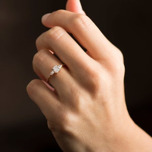 May include: A rose gold engagement ring with a square-shaped center diamond and two smaller pear-shaped diamonds on either side.