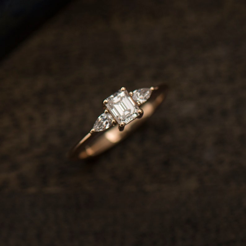May include: A gold engagement ring with a large emerald cut diamond and two smaller pear-shaped diamonds on the band.