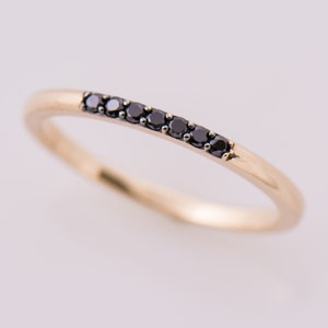 May include: A delicate gold band ring with a row of black diamonds.