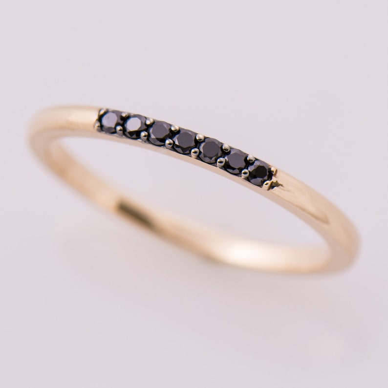 May include: A delicate gold band ring with a row of black diamonds.